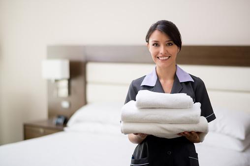 Smiling hotel staff holding neatly folded towels in a guest room.